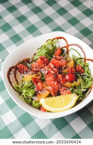 Italian salad with smoked salmon, broccoli, cherry tomatoes, orange slices and fresh basil. Concept for a tasty and healthy meal. Over green plaid tablecloth. Other food on the background.