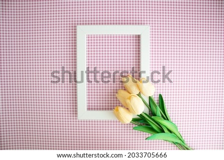 White frame and tulips on red white plaid background, space for text, celebration concept idea, top view