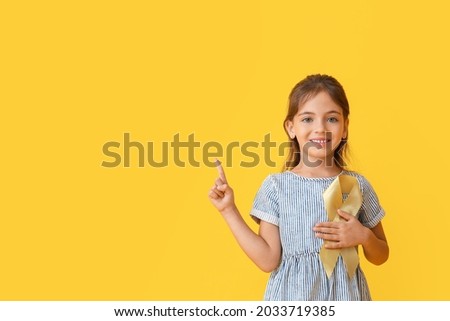 Little girl with golden ribbon showing something on color background. Childhood cancer awareness concept