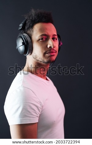 Smile Young African American man portrait wearing headphones and enjoy music over black Background. Red light reflection on face.