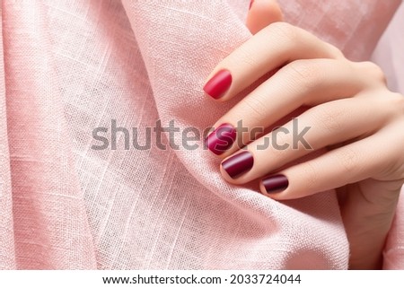 Female hand with red nail design. Perfect glitter red nail polish manicure. Red fingernails female hand on pink fabric. Beautiful female hand with perfect red manicure. Royalty-Free Stock Photo #2033724044