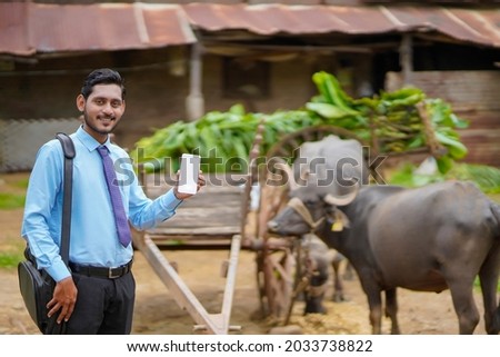 Young indian bank officer or agronomist showing smartphone at farmers house