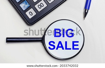 On a light background, a black calculator, a blue pen and a magnifying glass with text inside the word BIG SALE. View from above