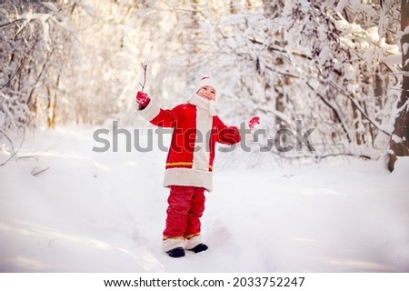 A pretty boy in a Santa Claus costume in a snowy forest for Christmas
