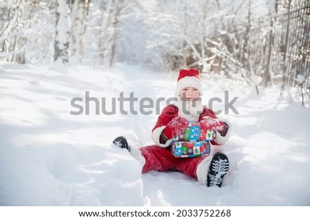 A pretty boy in a Santa Claus costume in a snowy forest for Christmas