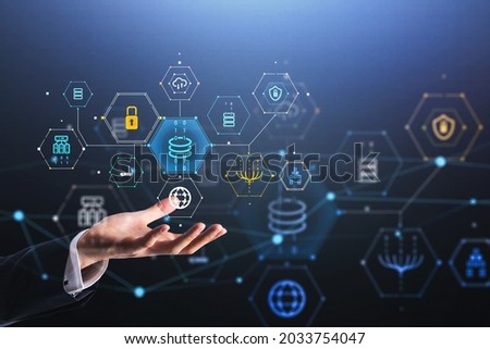 Businessman wearing formal suit is holding a digital interface in hand with hologram of globe, coin, padlock, cloud data storage. Dark blue background. Concept of internet security and protection