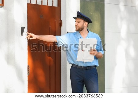 Handsome young postman ringing the door bell outdoors Royalty-Free Stock Photo #2033766569