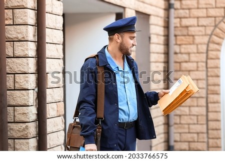 Handsome young postman with letters outdoors Royalty-Free Stock Photo #2033766575