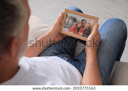 Senior man holding frame with photo of couple at home, closeup