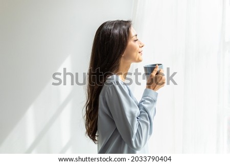 Slow motion Shot. Pretty young caucasian woman look at the scenery by the window and enjoying first morning coffee on sunshine. her enjoying pleasant memories. daily routine and relaxation time Royalty-Free Stock Photo #2033790404