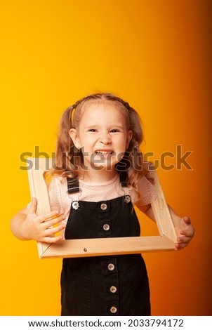 a little charming girl shows emotions holding a wooden frame in her hands