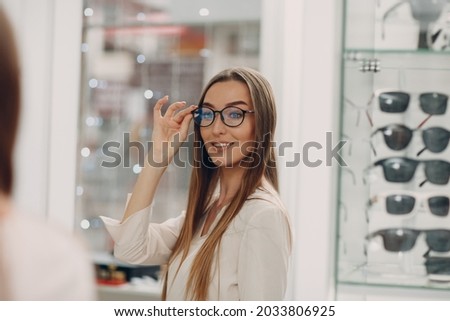 Close up of gorgeous young woman smiling picking and choosing glasses at the optician corner at the shopping mall. Happy beautiful woman buying eyewear eyeglasses at the optometrist. Royalty-Free Stock Photo #2033806925