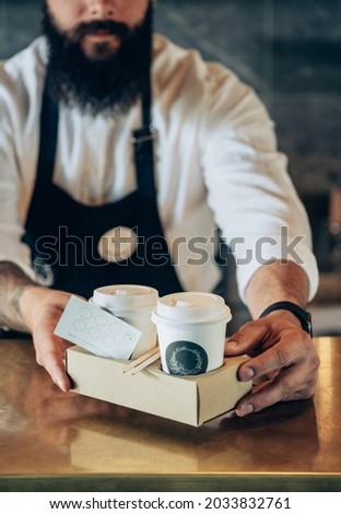 An Anonymous Barista Serving Two Take Away Paper Cup of a Coffee in a Cafe.
Close up photo of a waiter hands giving disposable tray with two cups of take out coffee with loyalty card in a coffee shop. Royalty-Free Stock Photo #2033832761