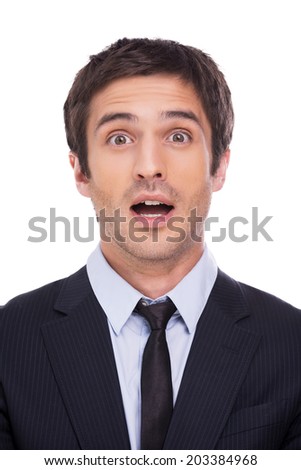 What a surprise! Surprised young man in formalwear staring at camera and keeping mouth open while standing against grey background