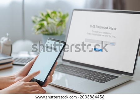 Woman hand holding phone showing security code for reset password and enters one-time password for the validation process on laptop, Mobile OTP secure Verification Method, 2-Step authentication. Royalty-Free Stock Photo #2033864456