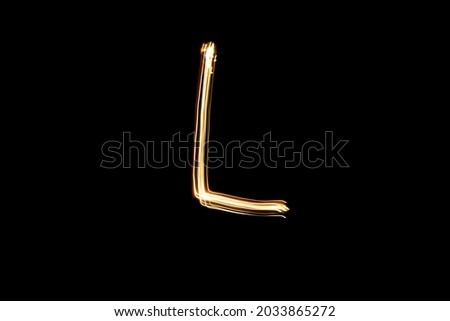 Letter L. Light painting alphabet. Long exposure photography. Drawn letter L with gold lights against black background.