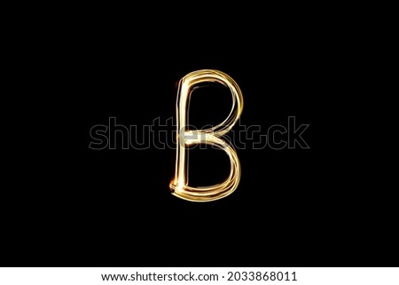 Letter B. Light painting alphabet. Long exposure photography. Drawn letter B with gold lights against black background.