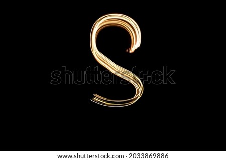 Letter S. Light painting alphabet. Long exposure photography. Drawn letter S with gold lights against black background.