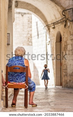 Grandmother waiting for her granddaughter on the doorstep in the narrow streets of Bari old town, Puglia, Italy, vertical