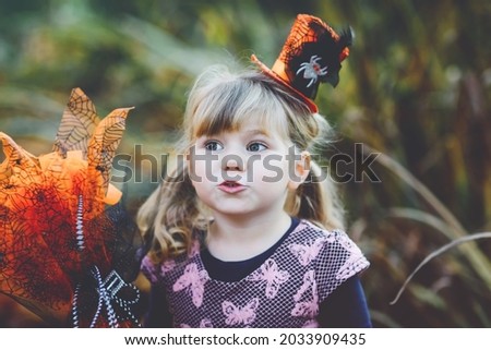Portrait of little toddler girl dressed as a witch celebrates Halloween. Happy child outdoors, with orange funny hat and hold witch broom. Beautiful family festival season in october. Outdoor activity