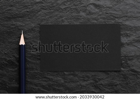 Black card and pencil on dark stone background.