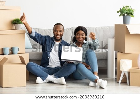 Happy Black Couple Holding Home Keys And Demonstrating Laptop Computer With Blank Screen After Moving To Their New Home, Joyful African American Spouses Recommending New Website, Mockup Image