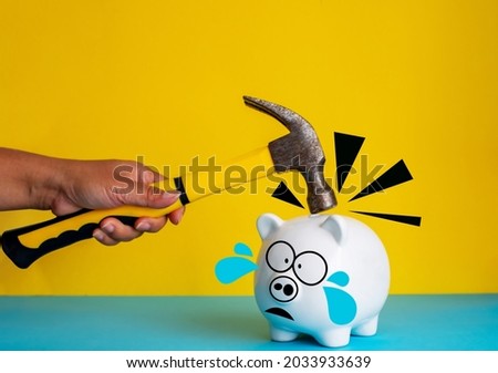 A woman's hand using hammer smash on piggy bank with scared face isolated on pink and blue background, copy space, business failure concept.

