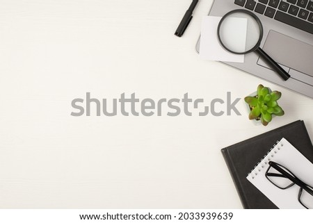 Top view photo of magnifying glass sticker note on grey laptop pen flowerpot and spectacles on two planners on isolated white wooden table background with empty space