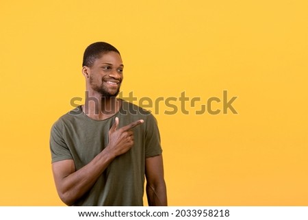 Positive black guy smiling and pointing aside at free space, isolated over yellow studio background. Excited black man aiming at advertisement, indicating copy space, banner