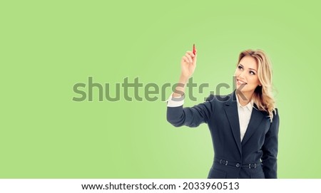 Smiling young businesswoman in grey confident suit, writing or drawing something on screen or transparent glass by marker, isolated over light green color background. Female executive. Business woman.