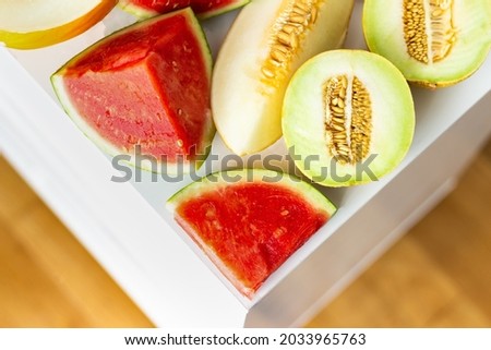 Close up of variety of cut melons forming a triangle on white and wooden background with copy space; summer fruit