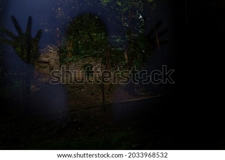 Halloween poster abstract concept picture with spooky ghost silhouette foreground and dark mystery wood land with gothic castle ruins background and empty copy for text on black space 
