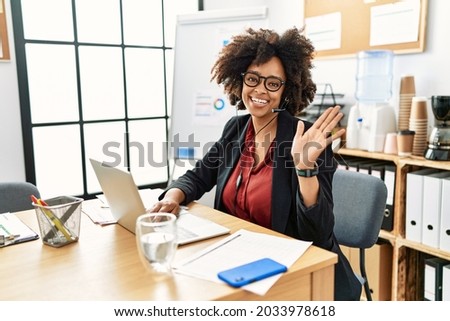 African american woman with afro hair working at the office wearing operator headset waiving saying hello happy and smiling, friendly welcome gesture  Royalty-Free Stock Photo #2033978618