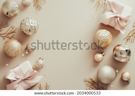 Christmas frame made of golden balls, decorative branches, gift boxes over beige background. Flat lay, top view. Xmas banner mockup with copy space