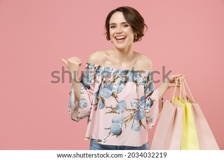 Young woman short hairdo wear trendy stylish blouse holding package bags with purchases after shopping point index finger back aside on workspace area mock up isolated on pastel pink background studio