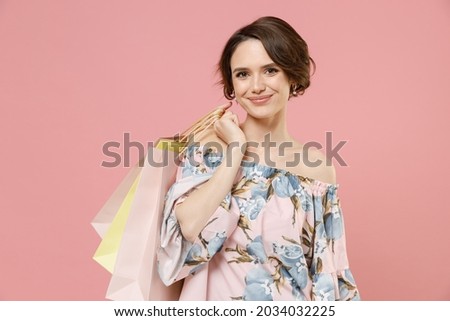Young excited smiling caucasian happy woman with short hairdo wear trendy stylish blouse holding package bags with purchases after shopping look camera isolated on pastel pink color background studio