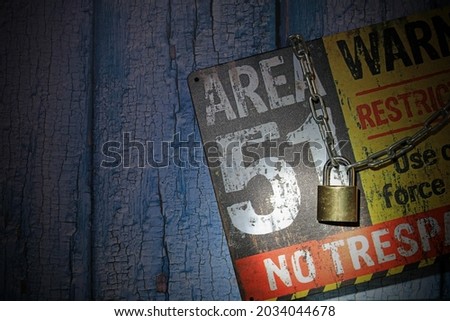 A Security Padlocked Chain Around An Area 51 Sign Lit By A Flash Light. Top Secret Concept. Royalty-Free Stock Photo #2034044678