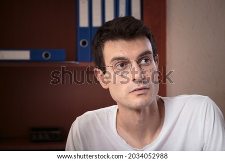 Portrait of a concentrated young man. The photo was taken in the office and there are folders in the background. Close-up.