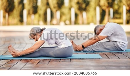 Active mature family man and woman doing yoga exercise seated forward bend while exercising in morning on fresh air, stretching back over legs, senior couple practicing Paschimottanasana Royalty-Free Stock Photo #2034085766