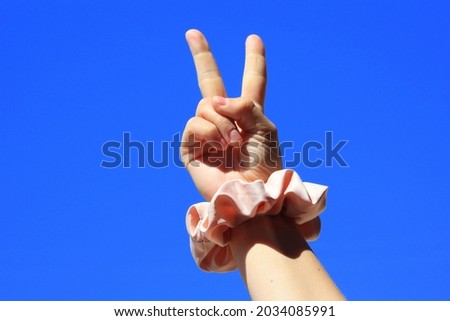 Hand up in the sky with a scrunchie on a wrist. Peace sign. 