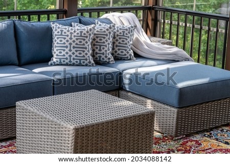 Close up of patio furniture in modern screened porch, summertime woods in the background.