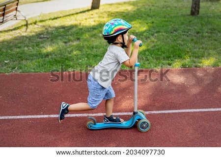 Profile view of cute blond little 4-5 years caucasian school boy wear helmet enjoy having fun riding kick scooter city street park outdoors on sunny day. Healthy sport children activities outside Royalty-Free Stock Photo #2034097730