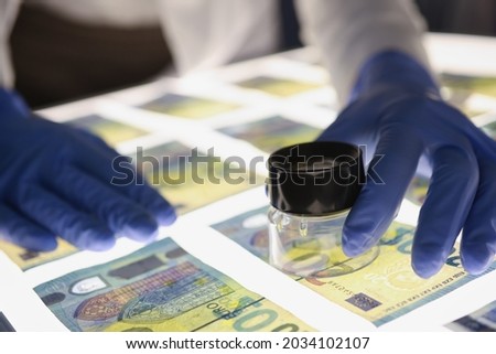 Man in rubber gloves checking authenticity of euro bills using lens closeup