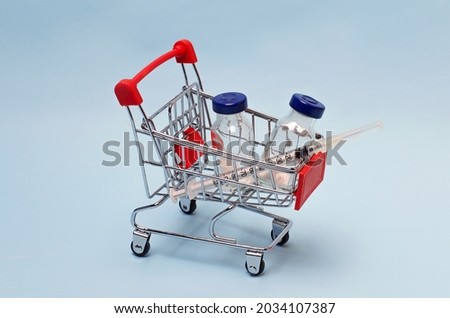 On a blue background, a supermarket trolley filled with a vaccine and a syringe. Place for text.Medical theme.Concept: home delivery of drugs and vaccines.Cart