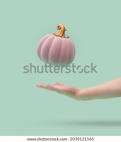 Pink Halloween pumpkin with golden petiole falling into women arm. Green mint background. Minimal design.