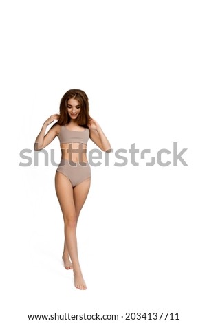 Young, fit and beautiful slender girl in gray sports underwear posing on a white background. Health care, diet, sport and fitness concept