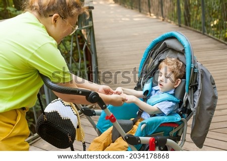 a little disabled boy in a wheelchair with his mother in a city park on a summer day. Infantile paralysis. Disability. Inclusivity. Restriction of movement.