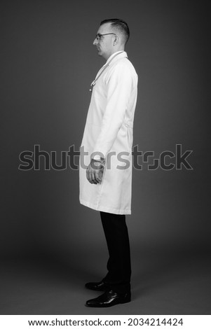Studio shot of man doctor wearing eyeglasses against gray background in black and white