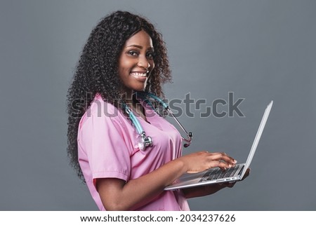An African doctor in a pink uniform with a stethoscope consults a patient, makes a video call from a webcam on a laptop. videoconference remote computer application virtual meeting.