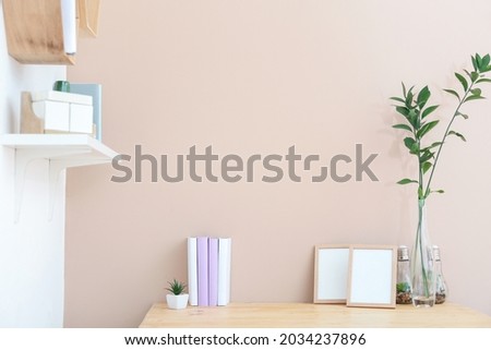 Books, frames and floral decor on table near color wall